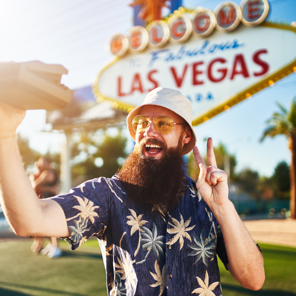 A bearded tourist takes a selfi in front of a Vegas sign